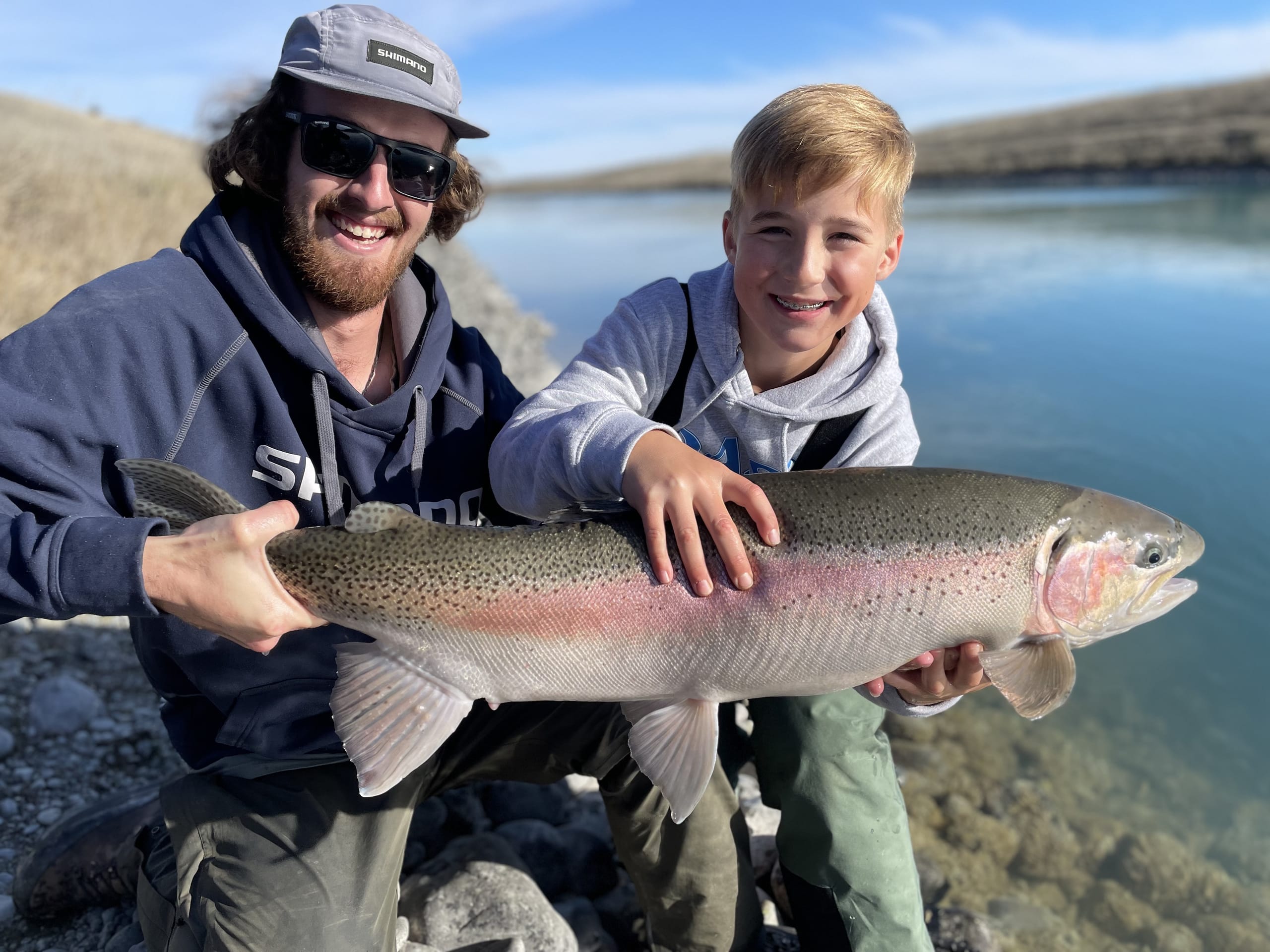 Guide and young angler holding a huge rainbow trout beside a Mackenzie canal