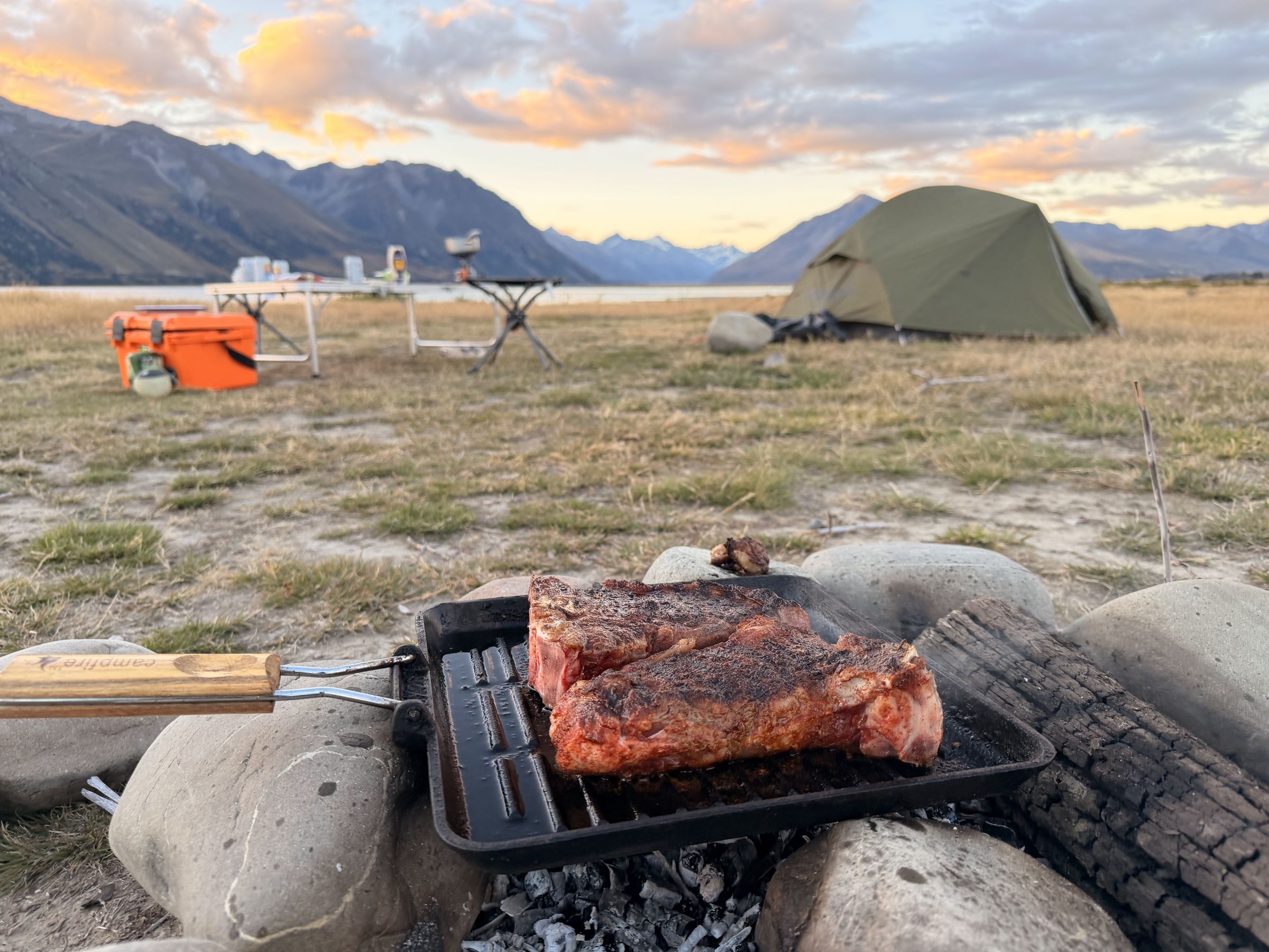 Lakeside campsite at sunset with steak cooking over the campfire